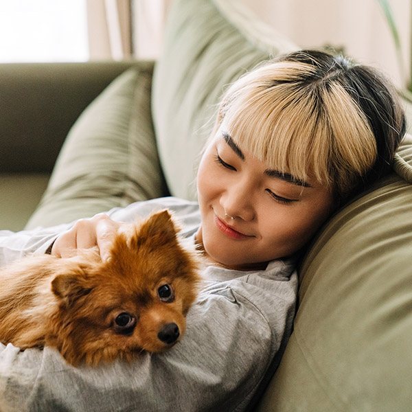 Person relaxing on a sofa with a small dog resting in their arms
