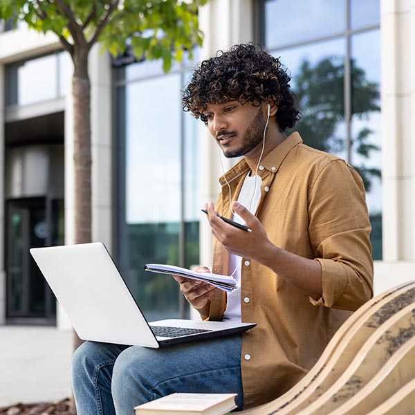 Man sits outside on a bench with a laptop and headphones