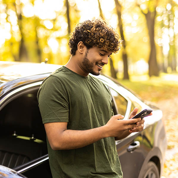 man standing by his car texting on mobile phone