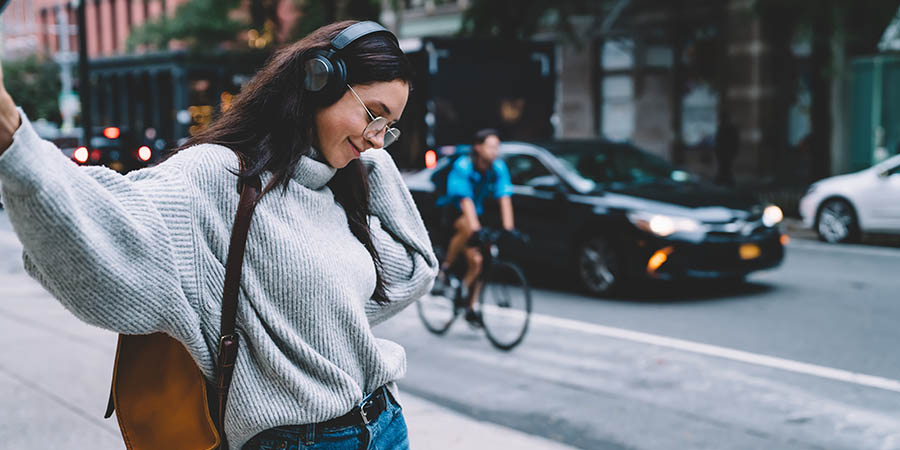 Young female walking on sidewalk and listening music