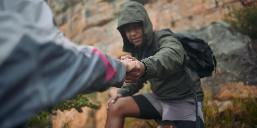 Shot of a man helping his partner up a cliff while mountain climbing