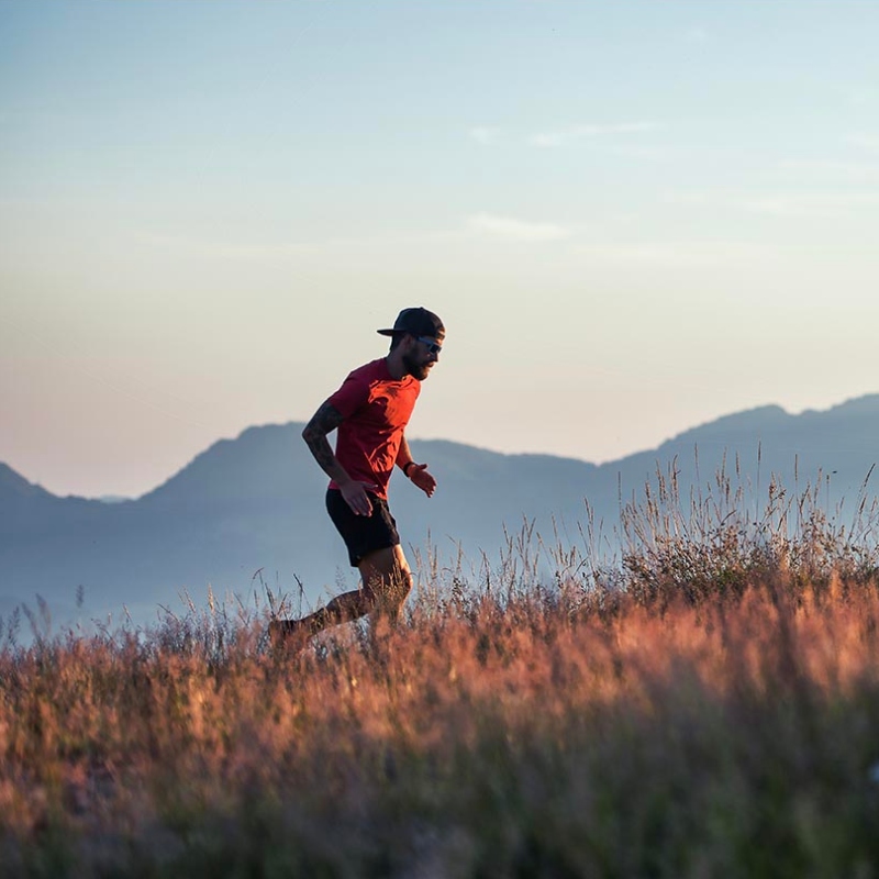 In a hilly sunset in colorful meadows a young sporty man runs alone