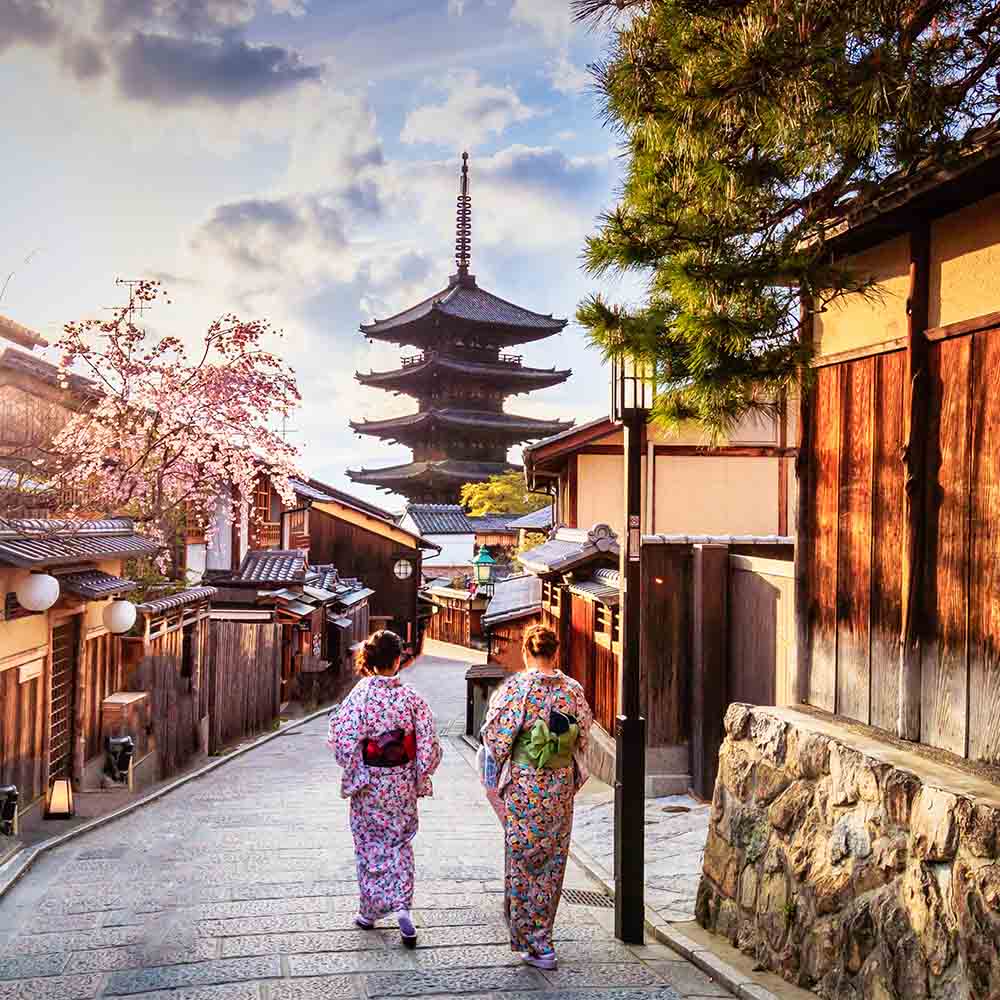 Visitors walking through a historic street lined with traditional buildings and a pagoda in the distance