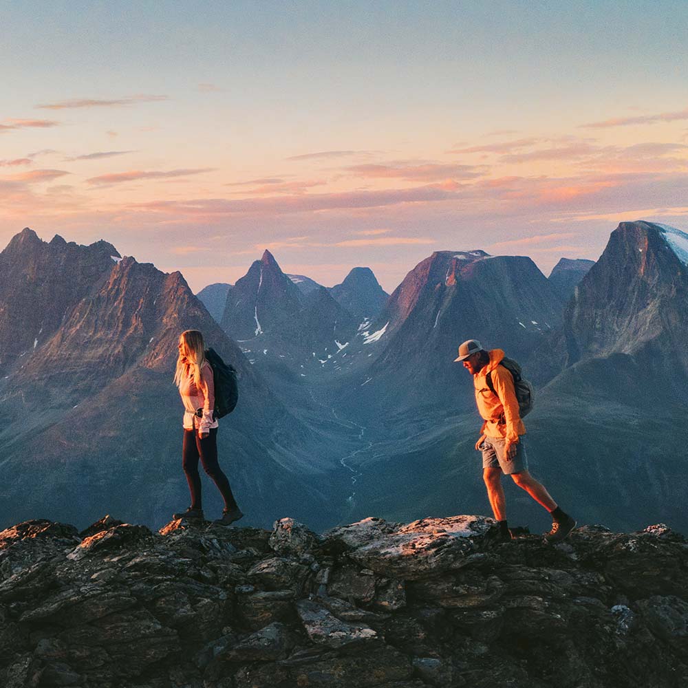 Two hikers crossing a mountain ridge at sunrise