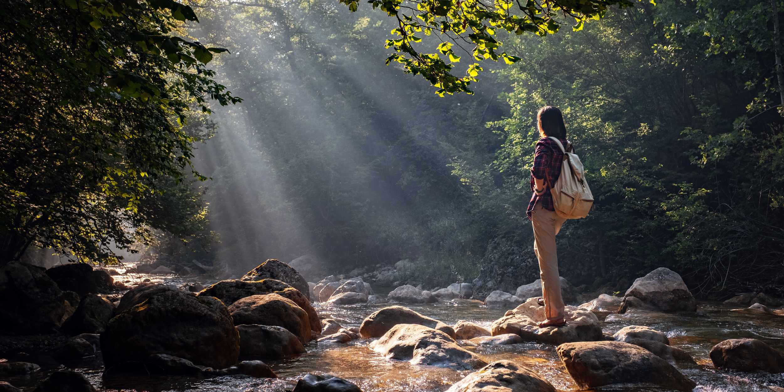 hiker standing on rocks by stream