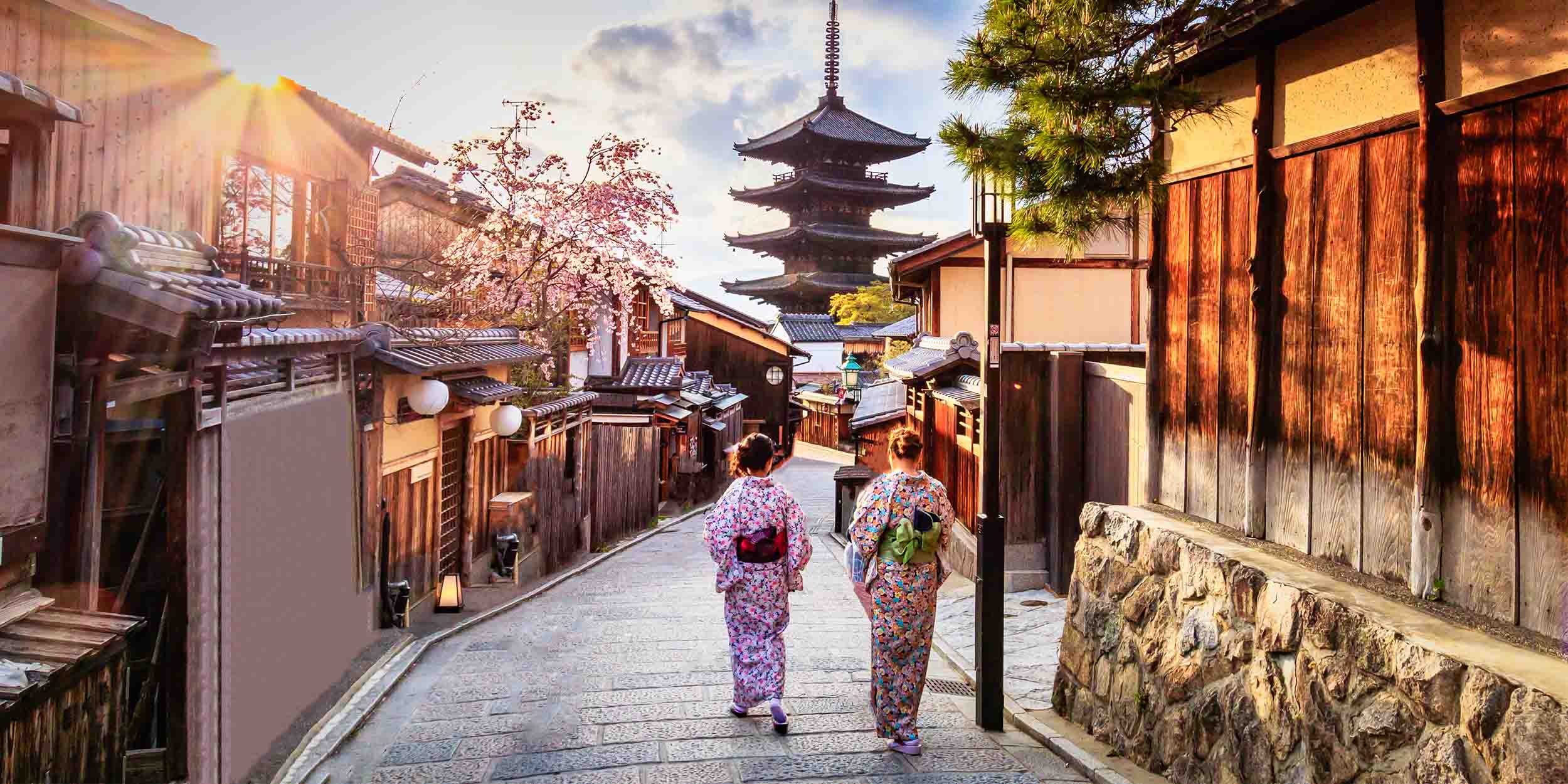 Visitors walking through a historic street lined with traditional buildings and a pagoda in the distance