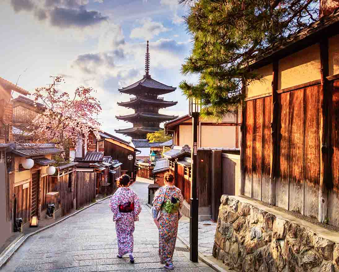 Visitors walking through a historic street lined with traditional buildings and a pagoda in the distance