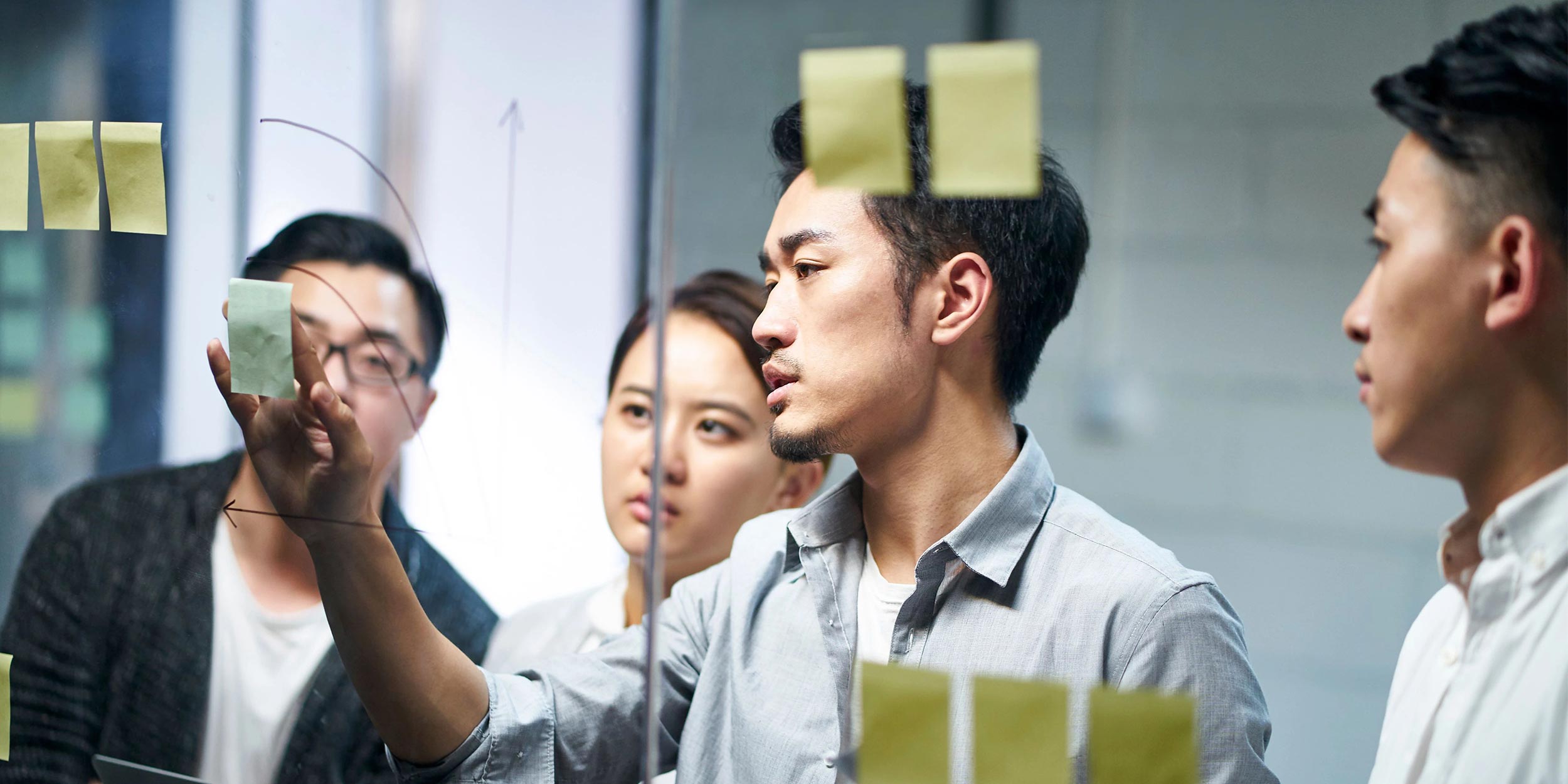 entrepreneur putting a note on glass during team meeting