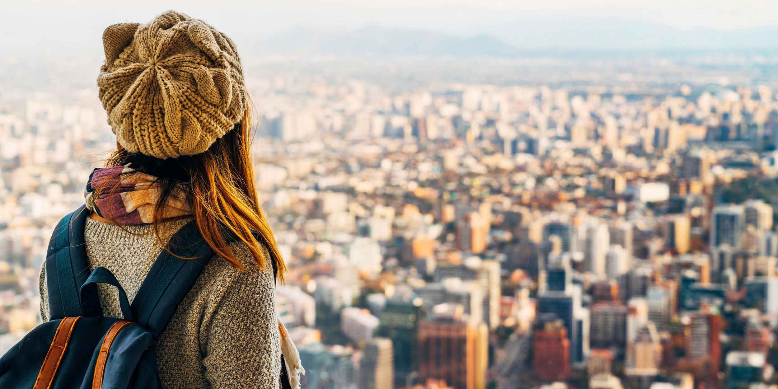 Woman with hat and backpack looking out over cityscape