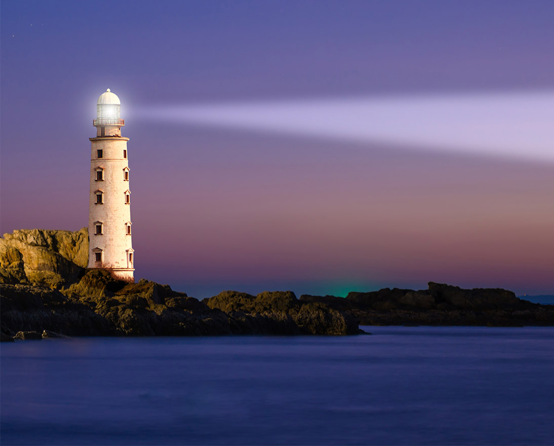 Lighthouse casting a beam of light across a rocky coastline at dusk