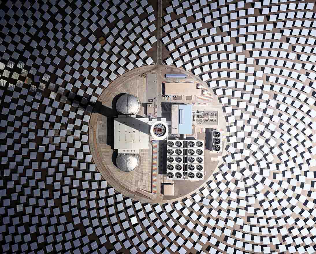 Aerial view of a solar power plant, with mirrors arranged in circular patterns around a central energy tower