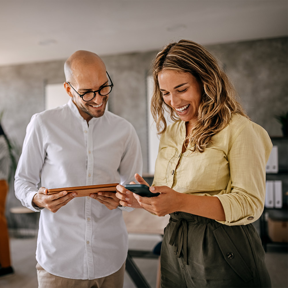 two colleagues looking at their phone and tablet together