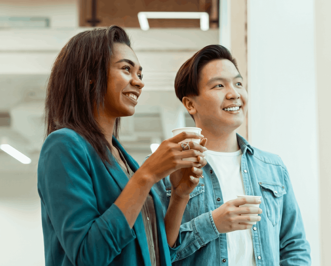 two colleagues holding coffee in office hallway