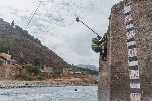 A technician installs a LiDAR station next to an old river measurement ruler on a bank of the Vilcanota River, Peru