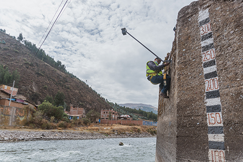 A technician installs a LiDAR station next to an old river measurement ruler on a bank of the Vilcanota River, Peru